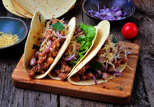 Three generously filled bean tacos on a wooden board